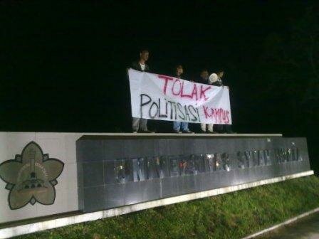 Beberapa mahasiswa yang sedang melakukan aksi demonstrasi dengan berorasi dan memegang selembar spanduk bertulis, "Tolak Politisasi Kampus" Senin (28/11/2011) malam di atas papan nama Unsyiah di kawasan pintu gerbang masuk Unsyiah, Simpang Galon, Darussalam. (Foto: Rahmat Taufik/DETaK)